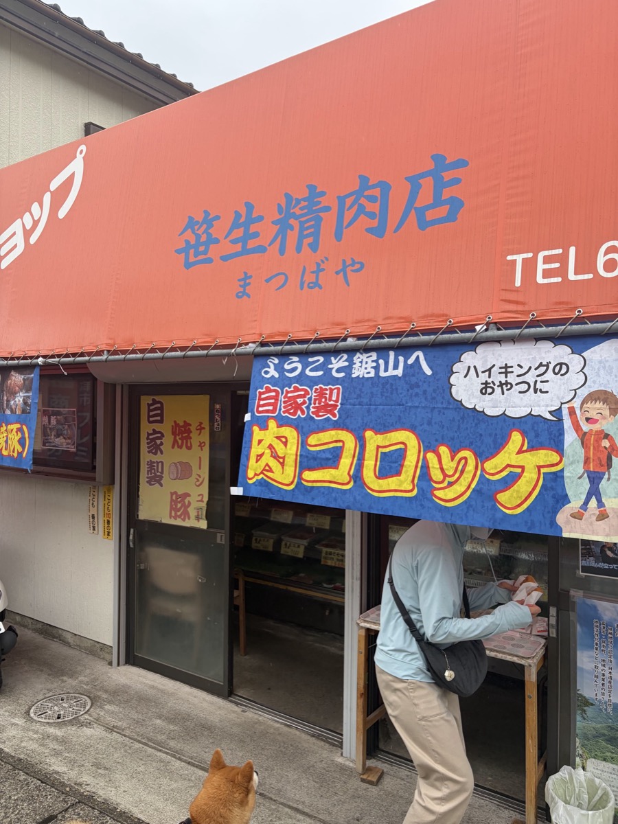 笹性精肉店の外観と暖簾、店の横にもみじが座っている
