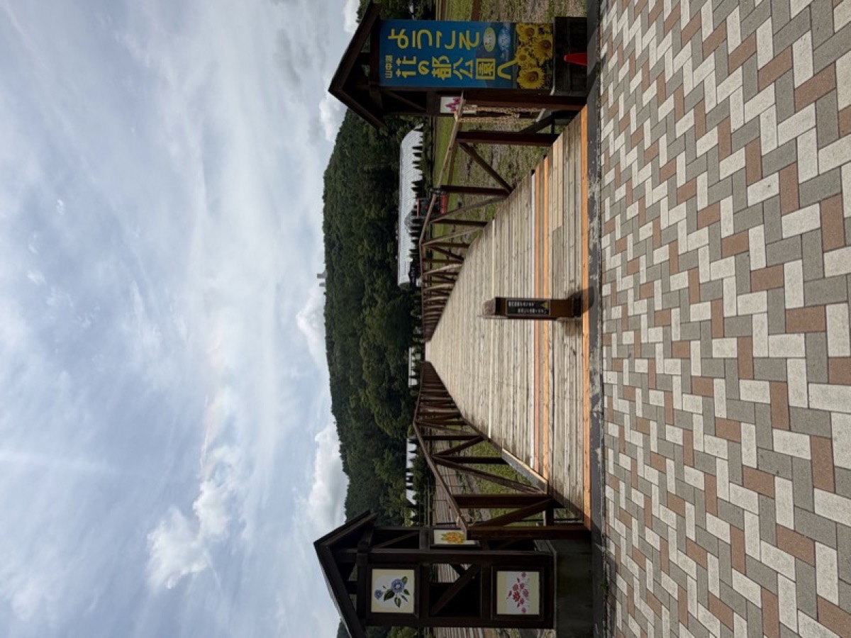 花の都公園入口の木の橋。「ようこそ花の都公園へ」と書かれた青い看板がある
