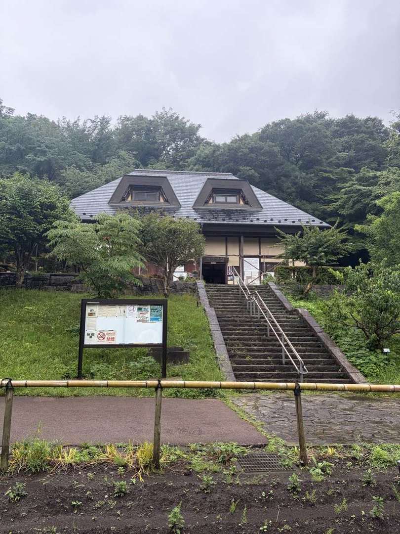 座間谷戸山公園の石段の上に建つ古民家風の建物。雨上がりの緑に囲まれている