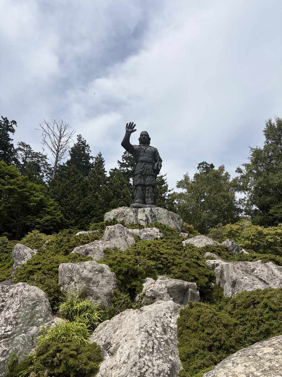 岩の上に立つ三峯神社の日本武尊(ヤマトタケル)像を見上げた写真