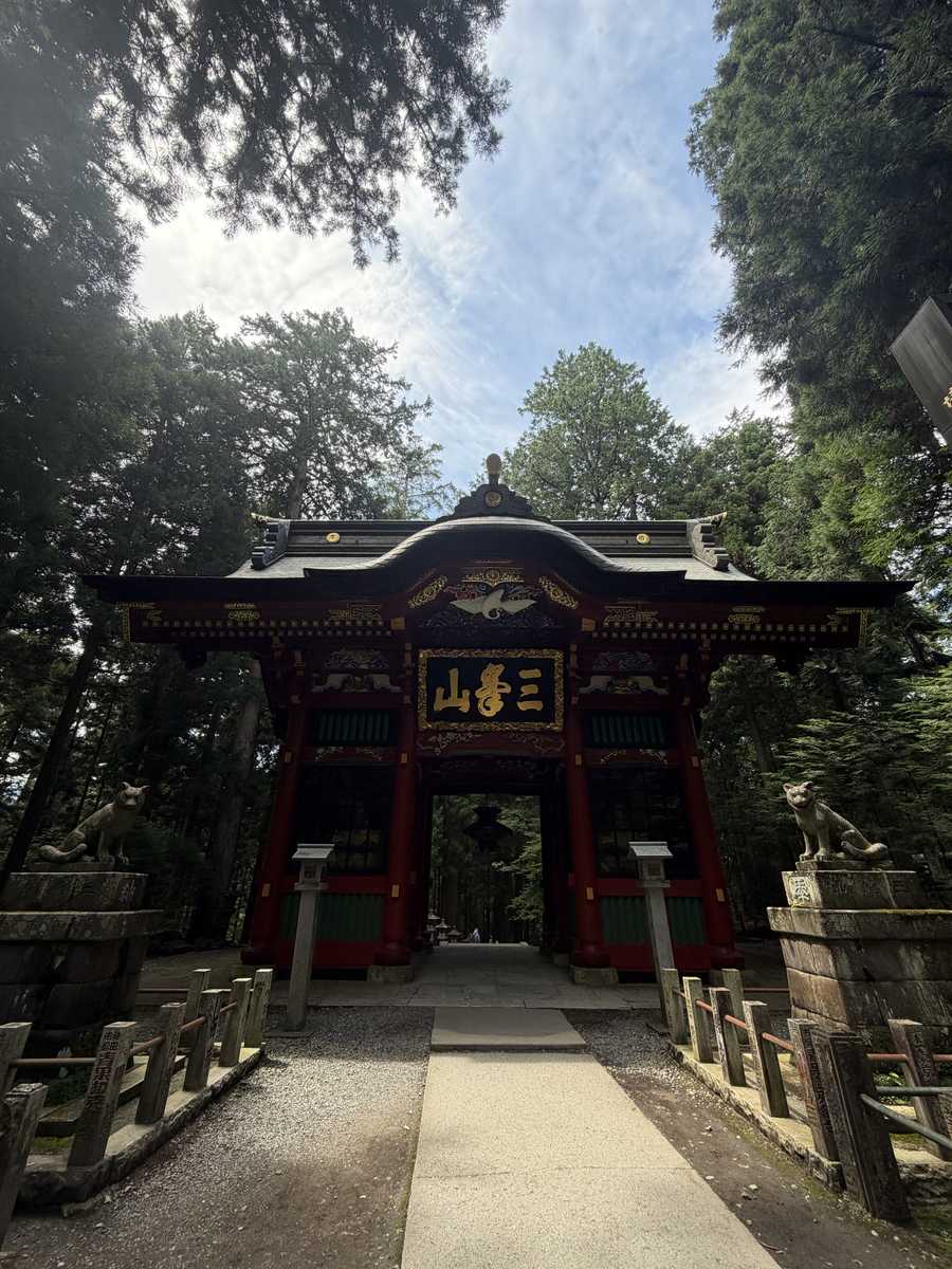 杉木立の中に立つ三峯神社の朱塗りの随身門