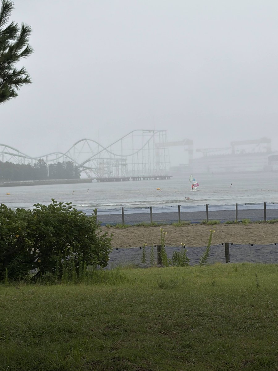 霧の海の向こうに八景島シーパラダイスのジェットコースターが見え、手前でウインドサーフィンをしている