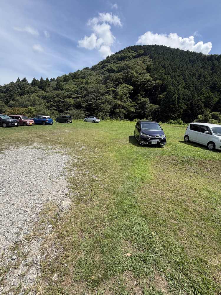 山あいの駐車場に停まった車と、その向こうに広がる緑の山と夏の青空
