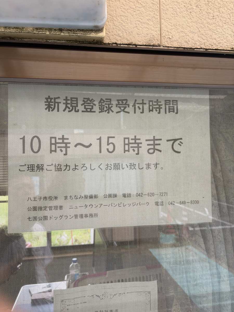 事務所の窓に貼られた新規登録受付時間の掲示。10時から15時までと書かれている